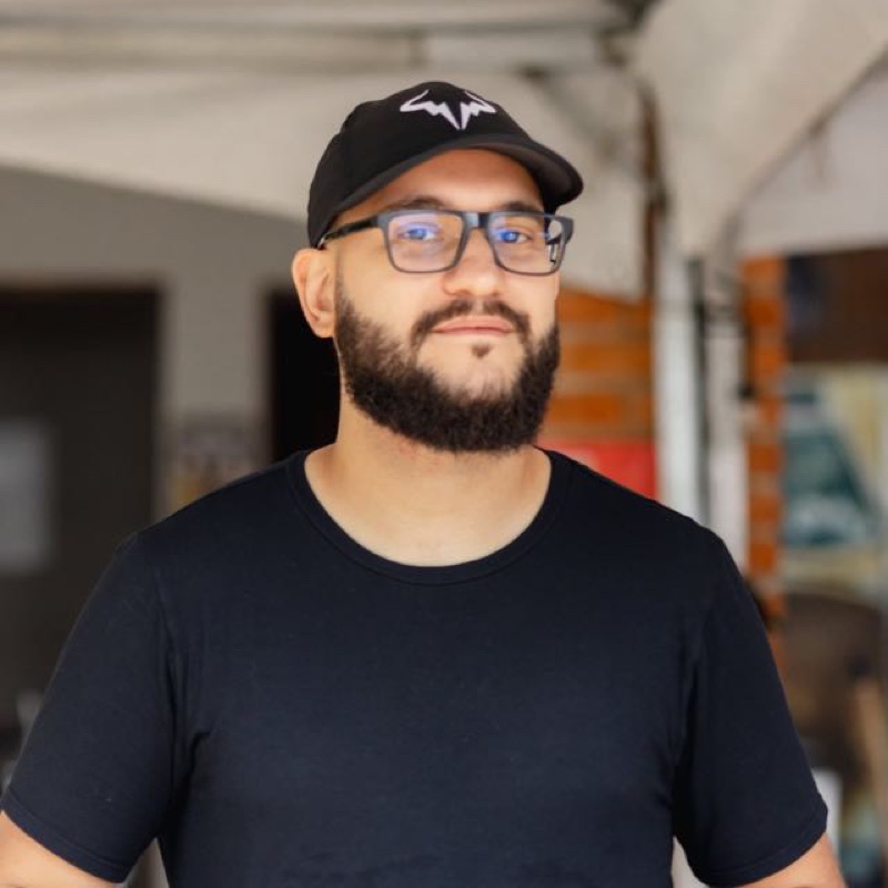 Felipe Maccheri sorrindo, com boné preto e óculos
